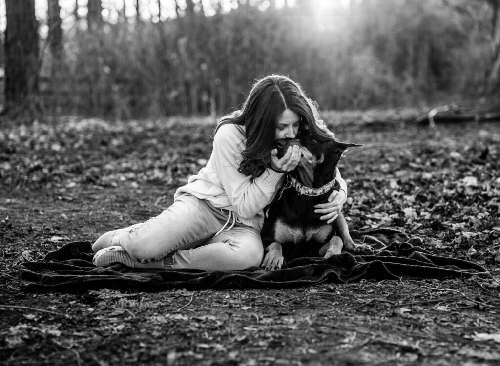 Woman sitting on blanket affectionately bonding with her dog in peaceful forest setting.