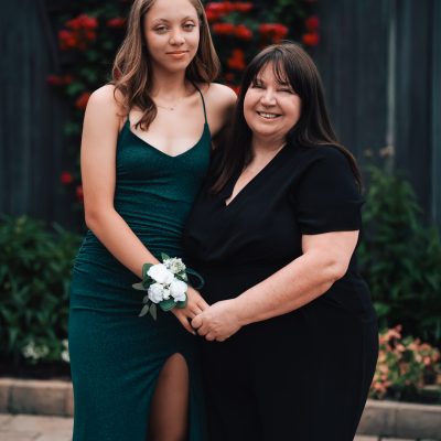 Mother and daughter share joyful graduation moment in elegant outfits surrounded by vibrant red flowers.