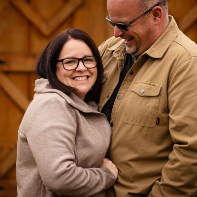 Happy couple smiling together in front of a rustic wooden barn door.