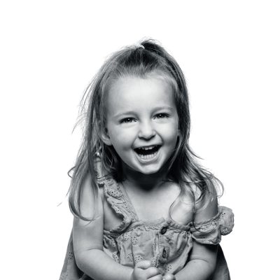 Smiling young girl laughing in black and white portrait, capturing pure childhood happiness.